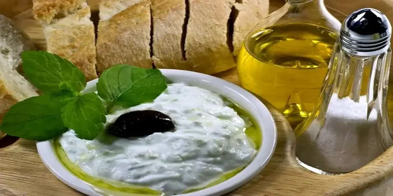 Tzatziki served in a bowl with olive oil, a black olive and fresh mint, alongside sliced bread.