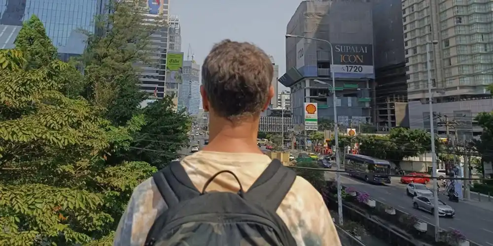 Backpacker looking across a busy Bangkok street surrounded by modern city buildings.