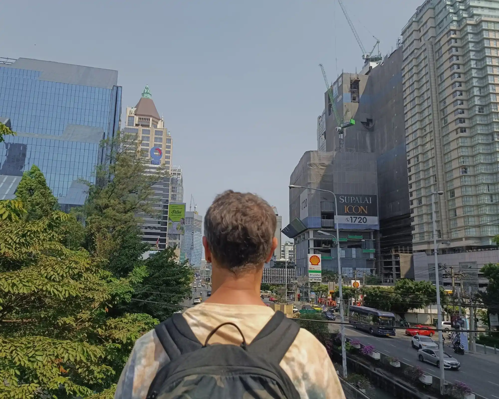 Backpacker looking across a busy Bangkok street surrounded by modern city buildings.