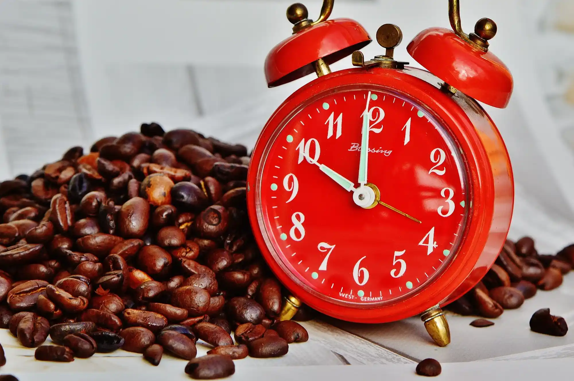 Jam alarm merah bergaya vintage di atas biji kopi sangrai, melambangkan ritme santai dalam gaya hidup santai.