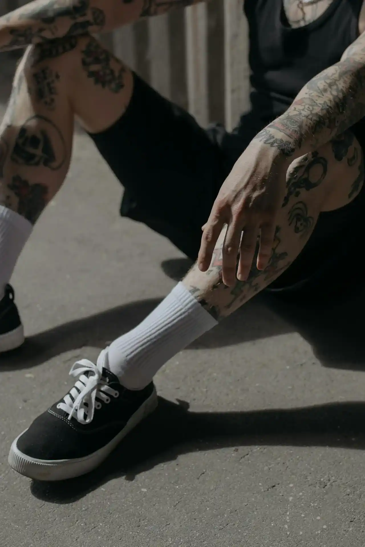 Seseorang mengenakan celana pendek hitam, kaos kaki putih tinggi dan sepatu hitam, dengan tato terlihat di kaki.