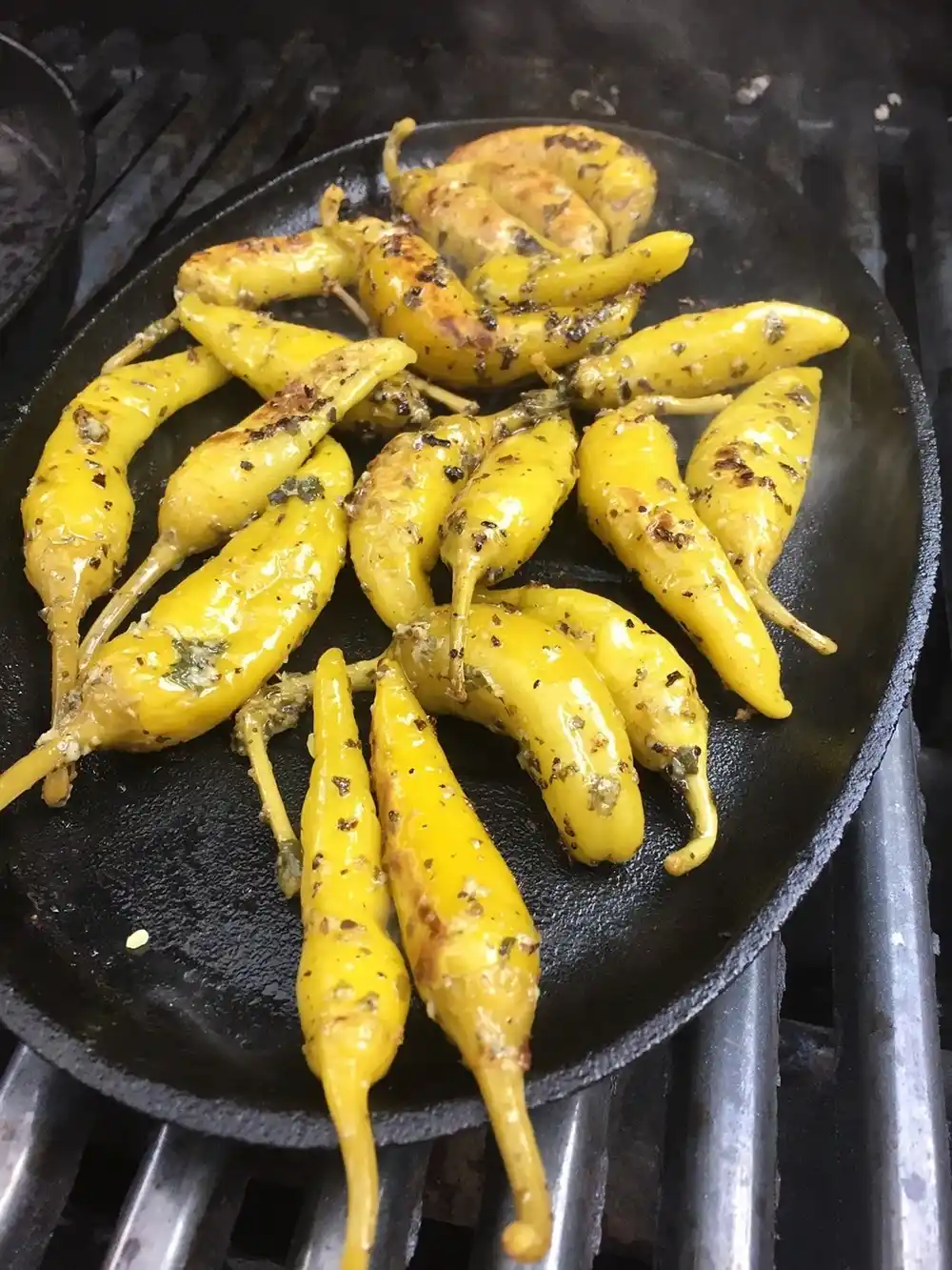 Grilled Greek peppers cooked in olive oil with herbs in a pan.