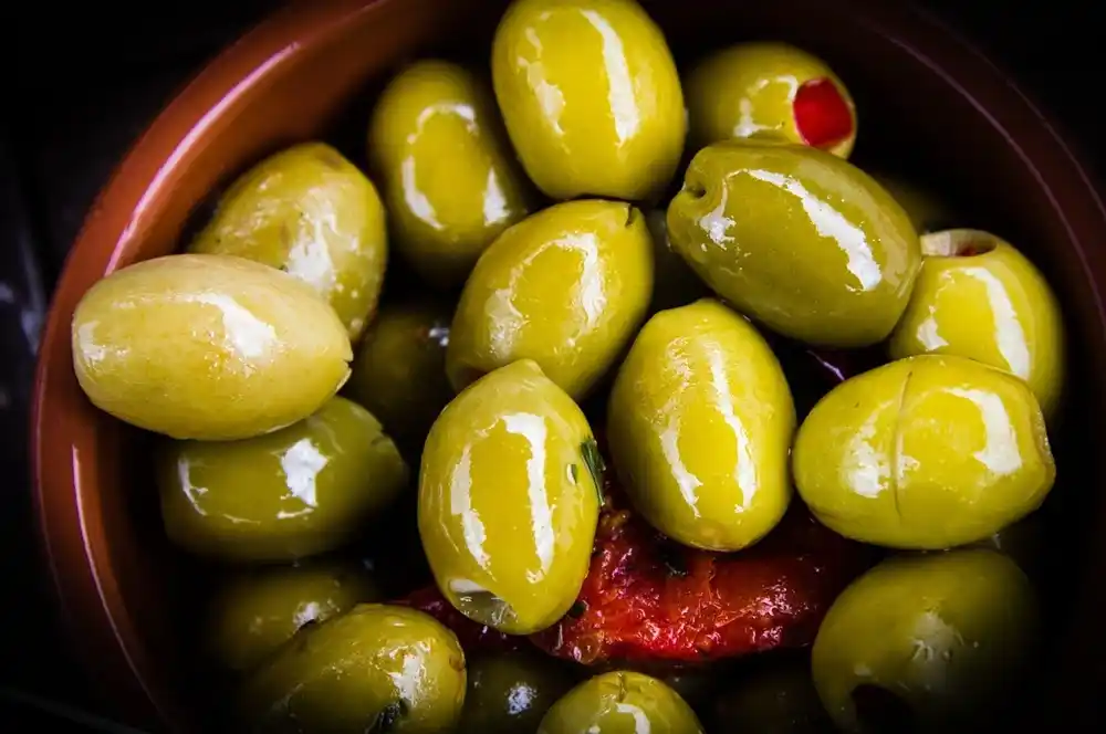 Close up of marinated green olives in olive oil with herbs and peppers.