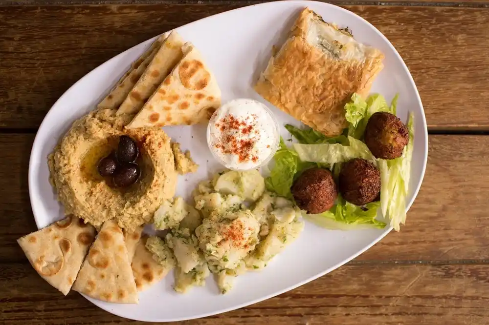 Greek meze platter with Hummus, Falafel, pita bread and side dishes served on a plate.