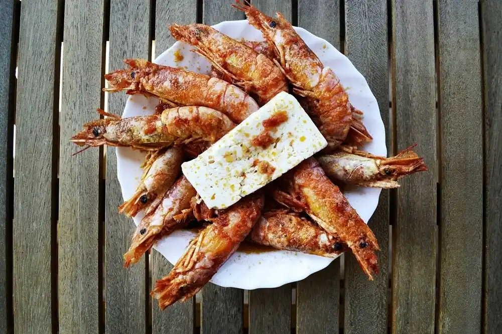 Grilled shrimp served with Feta cheese on a plate, typical Greek seafood dish.