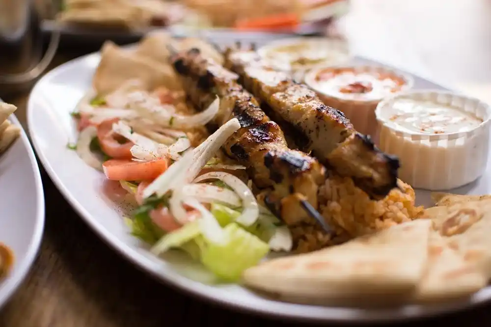 Greek Souvlaki skewers with pita bread, salad and dips served on a plate.