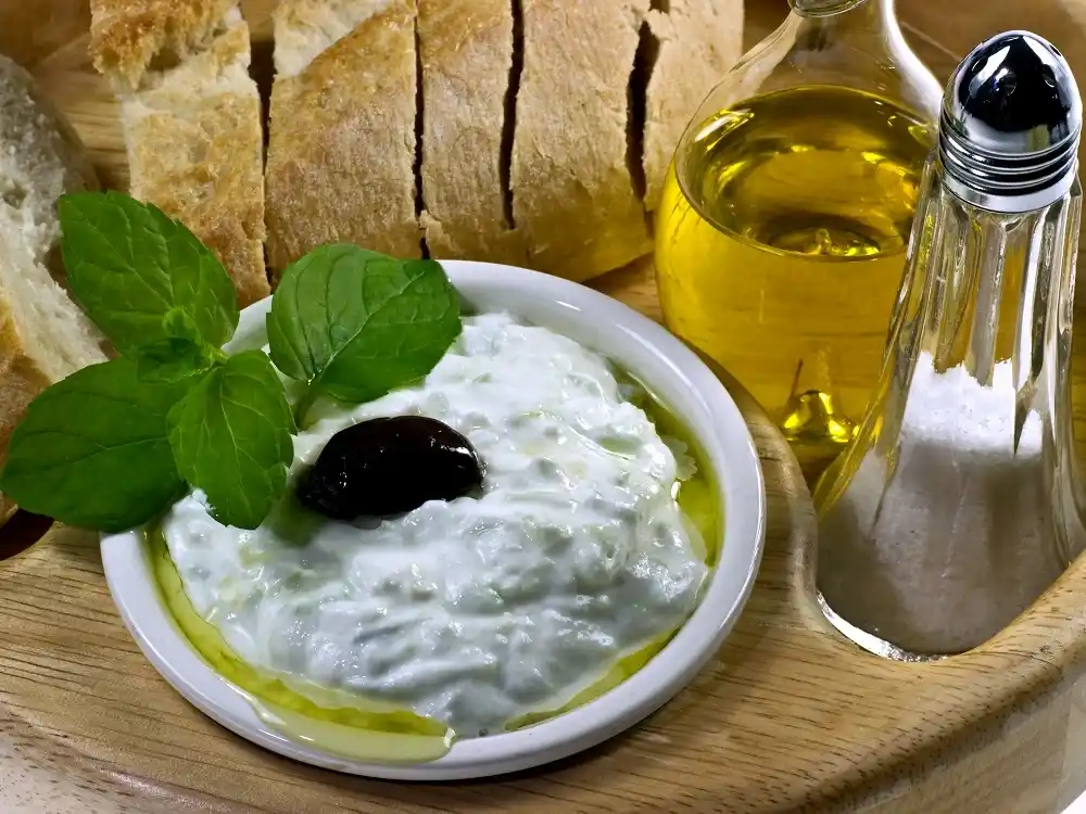 Greek Tzatziki dip with olive oil, bread and herbs served on a wooden board.