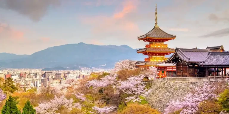 Kiyomizu-dera temple in Kyoto surrounded by cherry blossoms with city skyline in the background.