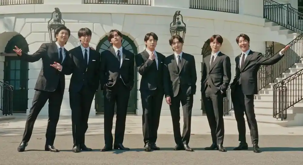 Seven-member K-pop group BTS standing together in formal suits outside a building.