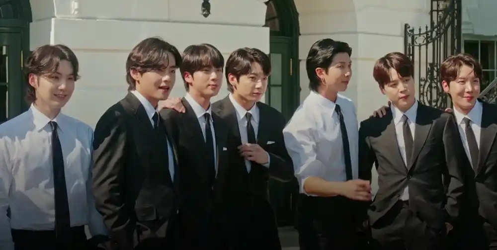 BTS members standing close together in suits, showing group chemistry and connection.