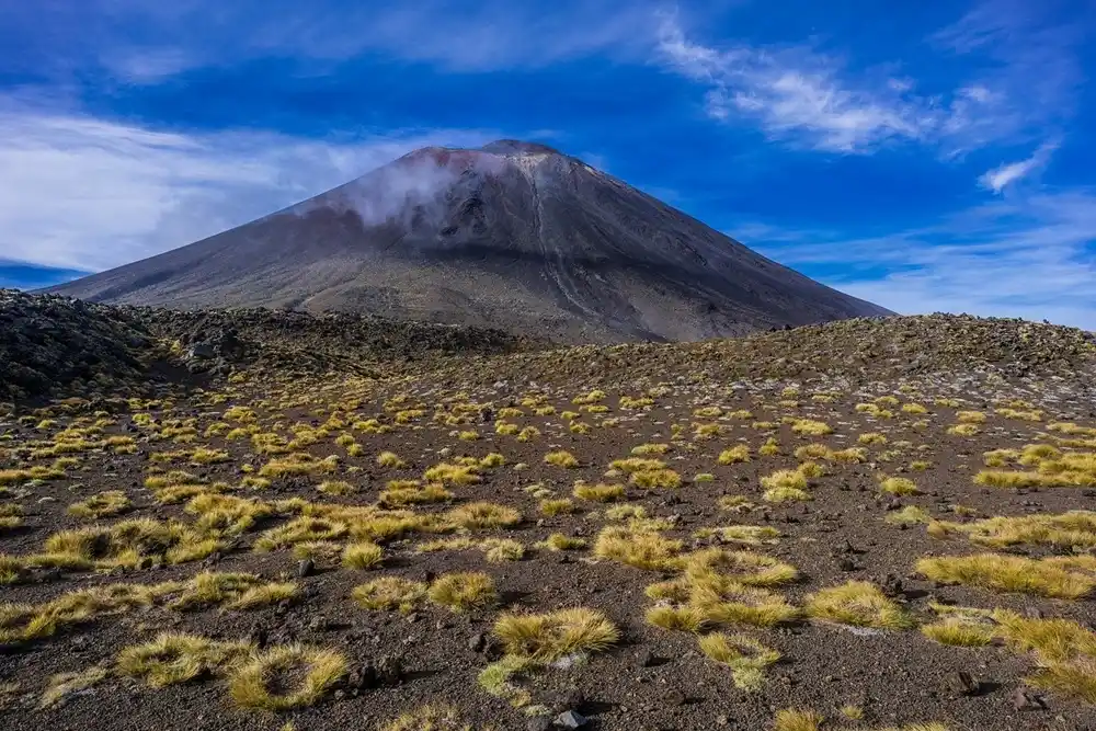 Mount Ngauruhoe in Tongariro National Park, New Zealand, with volcanic terrain and dry grasslands under a bright blue sky, known as the filming location for Mount Doom.
