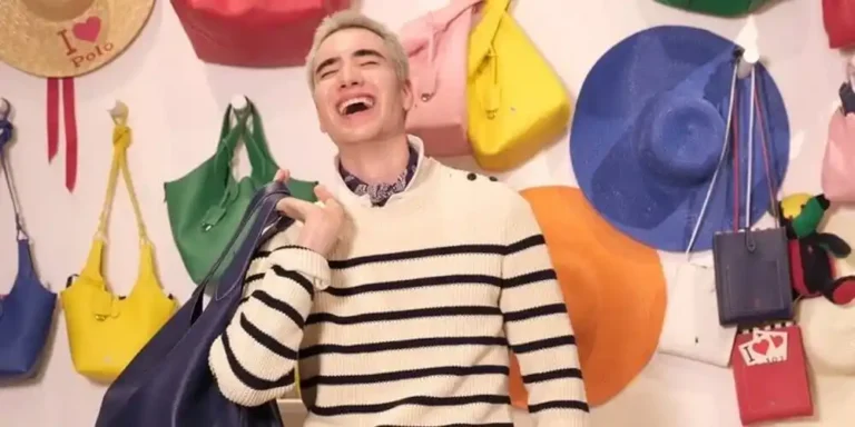 Lindow Ozaki wearing a striped jumper and white trousers, posing with a large navy handbag in front of a colourful handbag display.