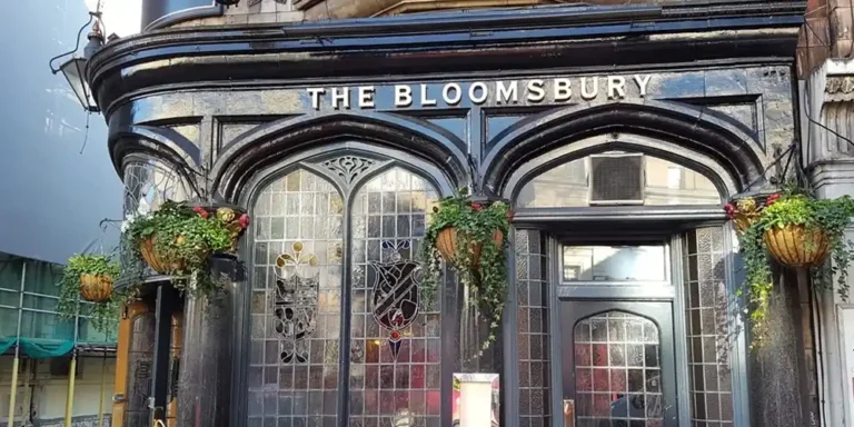 Historic Bloomsbury pub in London with dark wood facade, arched windows and hanging plants.